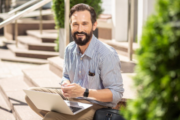 Joyful smiling man using laptop outdoors with pleasure
