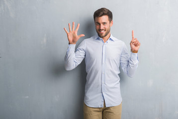 Handsome young business man over grey grunge wall wearing elegant shirt showing and pointing up with fingers number six while smiling confident and happy.