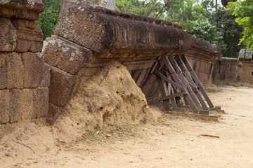 Wall ruin of ancient building with wooden scaffolding. Angkorian temple masonry restoration. Old sandstone wall debris