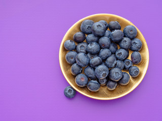 Healthy superfood blueberries on beautiful gold coloured plate, purple background.