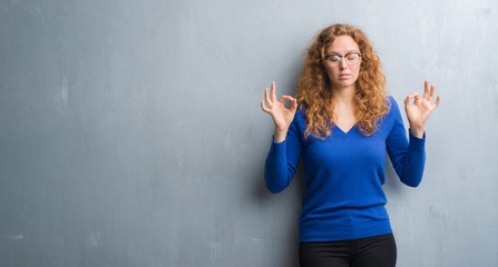 Young redhead woman over grey grunge wall relax and smiling with eyes closed doing meditation gesture with fingers. Yoga concept.