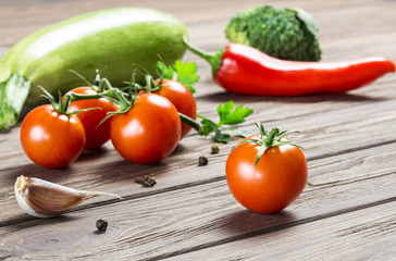 Ripe cherry tomatoes, garlic cloves, zucchini, greens, broccoli and a little pepper on a wooden surface.