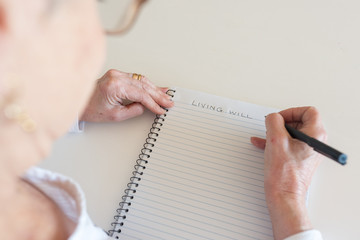 High angle view of older woman writing LIVING WILL in notebook (selective focus)