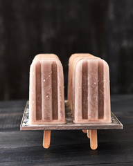 Homemade chocolate ice cream lolly in a plastic mold, on a black wooden background with copy space