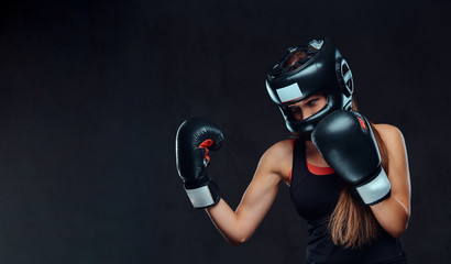 Sportive woman in sportswear wearing a protective helmet and boxing gloves, training in gym....
