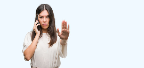 Young beautiful hispanic using smartphone with open hand doing stop sign with serious and confident...