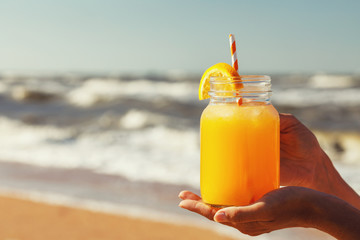 Orange juice with pulp in hands on the beach with space for text