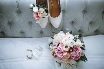 Brides wedding shoes with a bouquet with roses and other flowers on tha arm chair