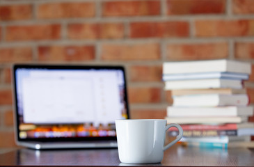 Cup of coffee and laptop computer on a table with books on brick wall background