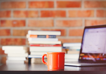 Cup of coffee and laptop computer on a table with books on brick wall background