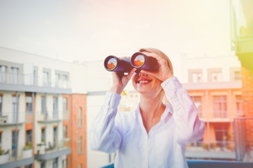 Beatiful girl with binocular looking for something with house on background.