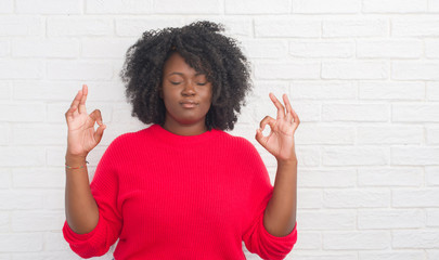 Young african american plus size woman over white brick wall relax and smiling with eyes closed doing meditation gesture with fingers. Yoga concept.