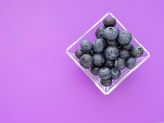 Healthy superfood blueberries in square glass bowl on beautiful purple background. With copyspace.