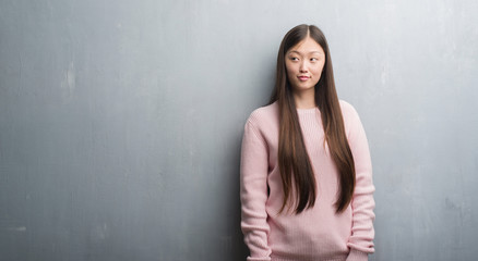 Young Chinese woman over grey wall smiling looking side and staring away thinking.