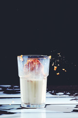 Homemade peanut cake fall to a glass of milk with splash on a black wooden table.