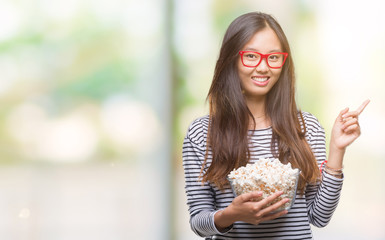 Young asian woman eating popcorn over isolated background very happy pointing with hand and finger to the side