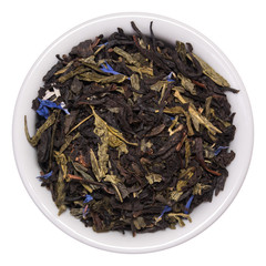Mix of black tea with green sencha tea and cornflower flowers and strawberry slices in white bowl on white background