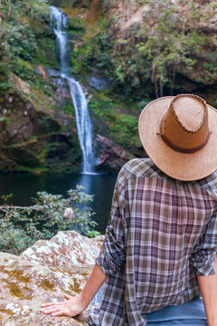 Back view of young girl in straw hat and looking at waterfall. Caucasian young lady looks at falling water, photo on fresh air. youth adolesce in wild nature