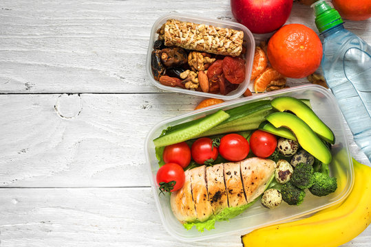 school lunch boxes with chicken, avocado, eggs and fresh vegetables, bottle of water, nuts and fruits