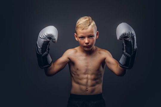 Young shirtless boy boxer with boxing gloves posing in a studio.