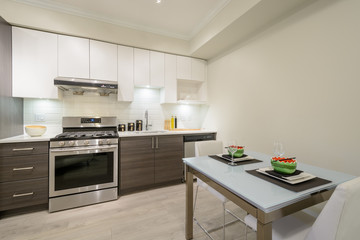 Modern, bright, clean kitchen interior with stainless steel appliances and dinner table in a luxury apartment.