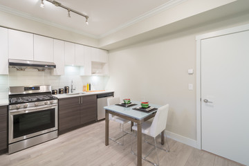 Modern, bright, clean kitchen interior with stainless steel appliances and dinner table in a luxury apartment.