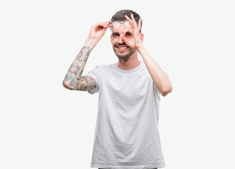 Fototapeta premium Young tattooed adult man doing ok gesture with hand smiling, eye looking through fingers with happy face.