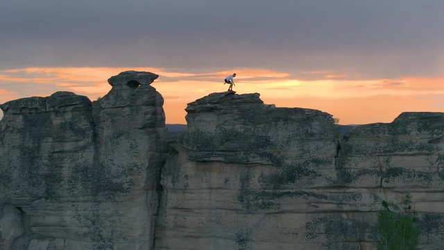 Side view of sportive anonymous man running and jumping extremely on top of long cliff against sunset sky