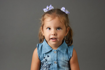 Happy face funny child girl in a blue dress. Portrait of adorable smiling little cute girl child with bow on her head isolated on gray background with copy space.