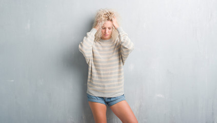 Young blonde woman with curly hair over grunge grey background suffering from headache desperate and stressed because pain and migraine. Hands on head.