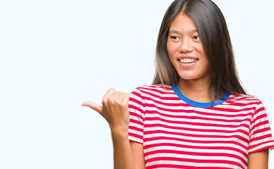 Young asian woman over isolated background smiling with happy face looking and pointing to the side with thumb up.