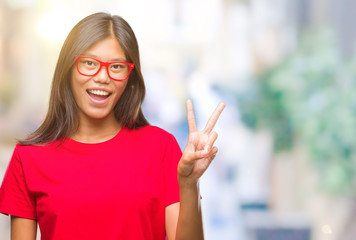 Young asian woman wearing glasses over isolated background smiling with happy face winking at the camera doing victory sign. Number two.