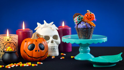 Happy Halloween candyland drip cake style cupcakes with lollipops and candy on blue background.