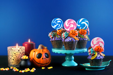 Happy Halloween candyland drip cake style cupcakes with lollipops and candy on blue background.