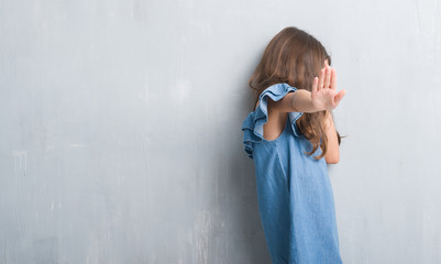 Young hispanic kid over grunge grey wall covering eyes with hands and doing stop gesture with sad...
