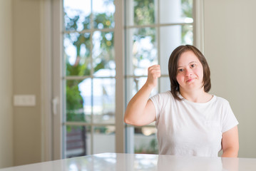 Down syndrome woman at home angry and mad raising fist frustrated and furious while shouting with anger. Rage and aggressive concept.