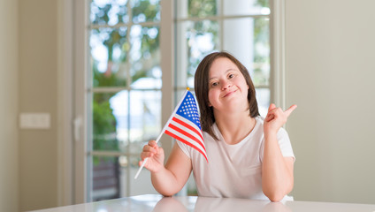 Down syndrome woman at home holding flag of usa very happy pointing with hand and finger to the side