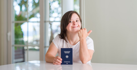 Down syndrome woman at home holding german passport pointing and showing with thumb up to the side...