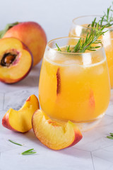 Homemade peach juice with ice cubes and rosemary leaves in glass on marble stone background.