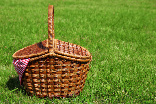 Wicker basket on green lawn prepared for picnic in park