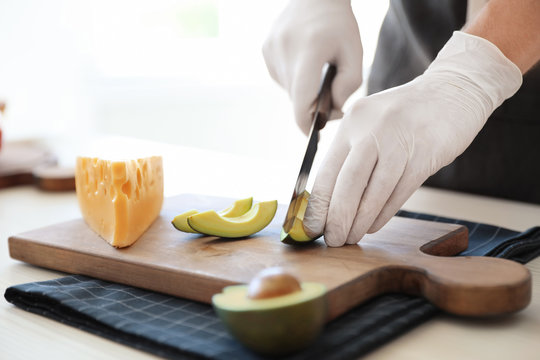 Professional chef cutting avocado on table in kitchen, closeup