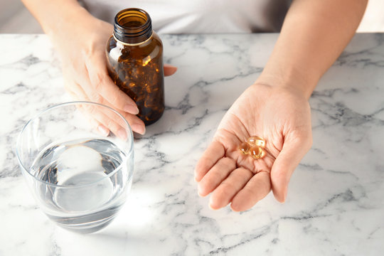 Woman with fish oil pills at table, closeup