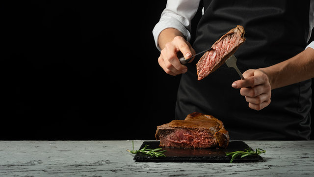 Chef, cut with a meat steak on a black background with an open space for text or restaurant menus. Horizontal photo Black text area. - Powered by Adobe