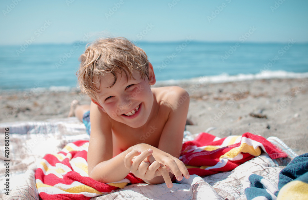 Wall mural a happy boy smiling on a colorful towel at the beach in summer