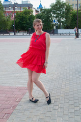 The Russian woman in a red dress walks and has fun in the park in the summer