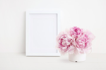 minimalist female mock up with white photo / picture frame and beautiful pink peonies in an enamel...