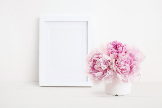 minimalist female mock up with white photo / picture frame and beautiful pink peonies in an enamel mug on a white desk, portrait format