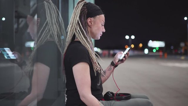 Young beautiful woman with dreadlocks using a smartphone outdoors at night