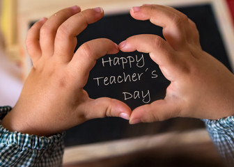 happy teachers day written on blackboard with students hand making a heart