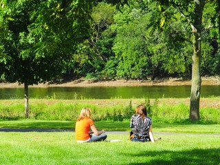 Friends Sitting On The Grass Enjoying The River's View